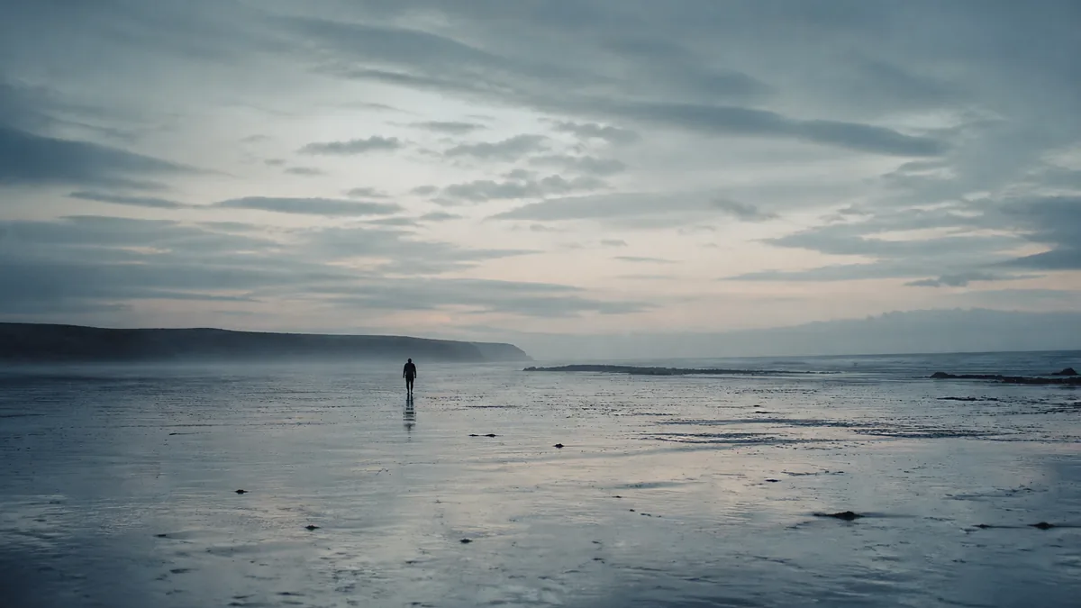 Filmstill eines Themenkurzfilms: eine einsame Figur auf einem leeren Watt unter weitem Abendhimmel (Bild: KI-generiert, gekennzeichnet nach Art. 50 EU AI Act)